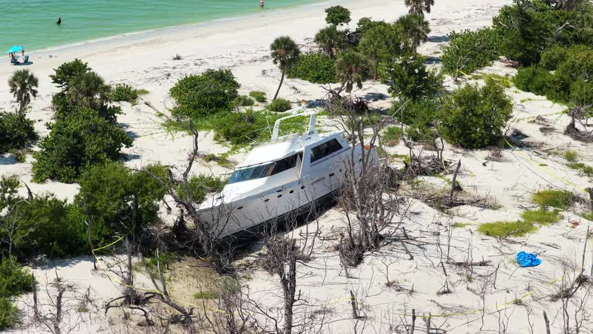 White boat stranded among dunes and sparse vegetation with beach and turquoise sea in the background
