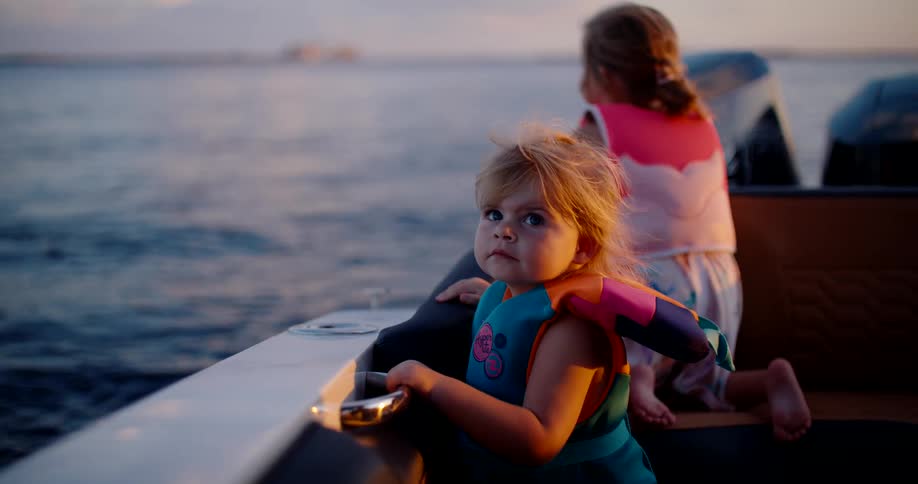 Children wearing life jackets watch the horizon during a boat ride at sunset