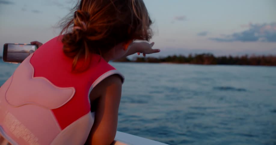 Little girl pointing toward the horizon on a boat during sunset