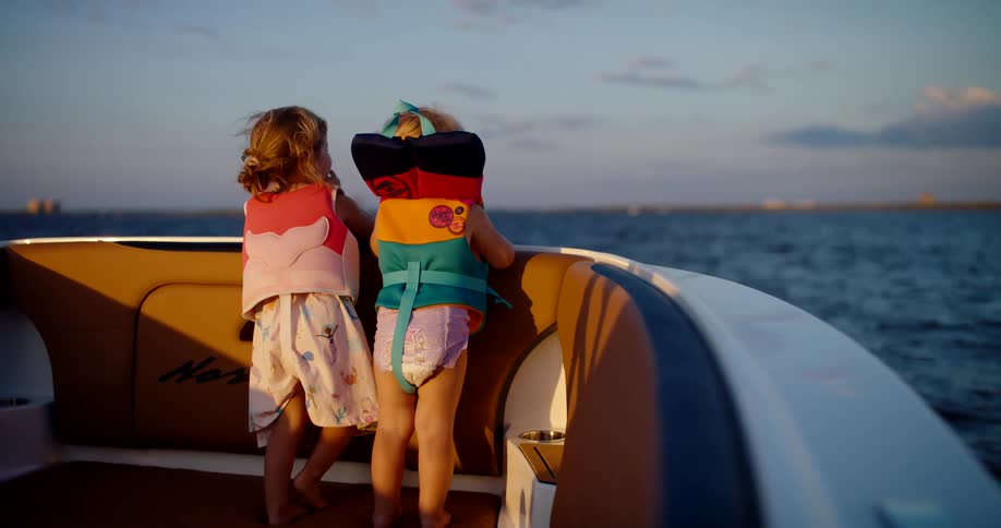 Children wearing life jackets watch the sea in the late afternoon aboard a boat