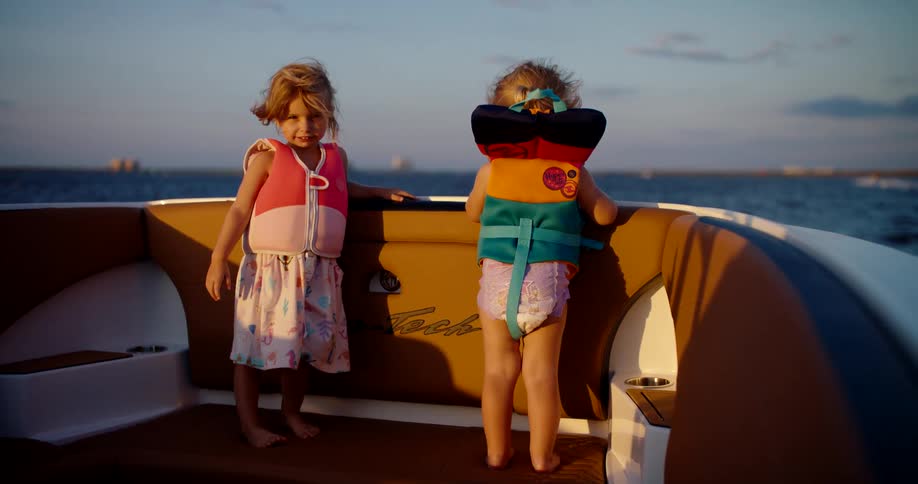 Two children wearing life jackets enjoy a boat ride at sunset