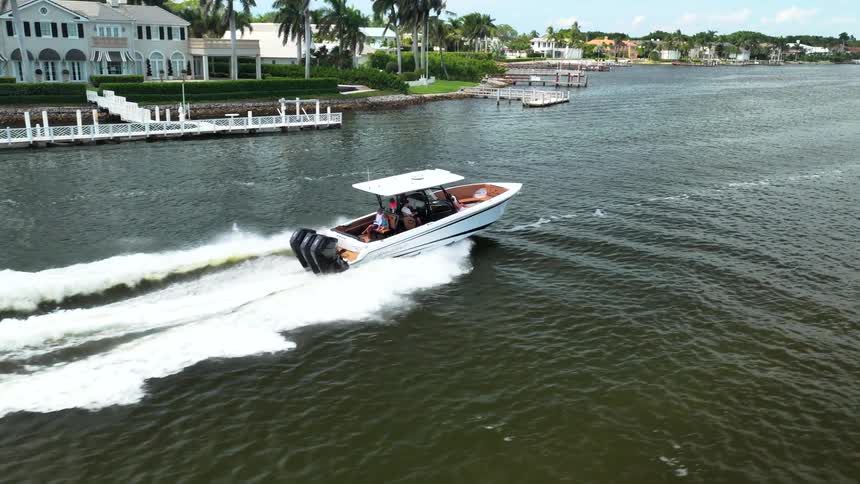 Speedboat accelerates through a canal surrounded by houses and palm trees in a residential area