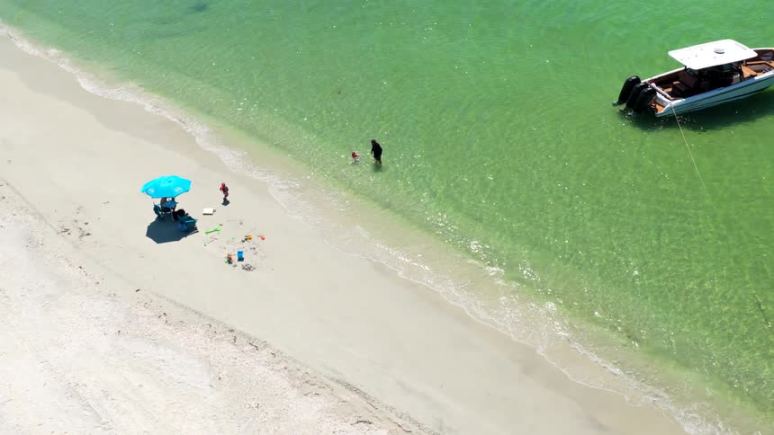 Peaceful beach with blue umbrella scattered toys and anchored boat in green water
