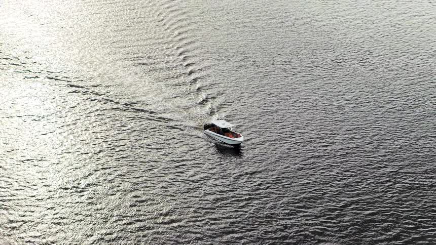 A small white motorboat cuts a vshaped wake across rippled silvery water viewed from above