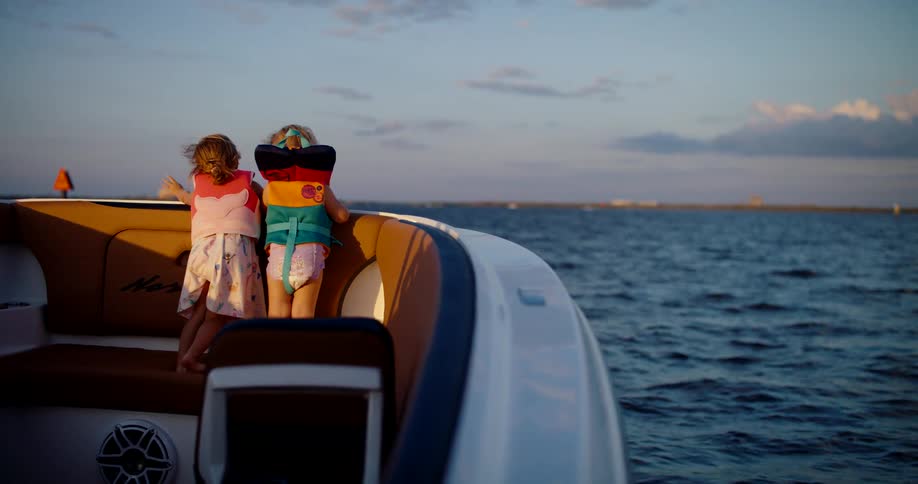 Children wearing life jackets look at the horizon aboard a speedboat