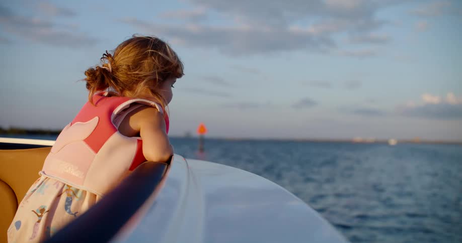 Little girl in pink life jacket looking at the water from the edge of a boat