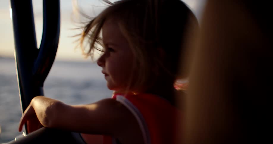 Child wearing a life jacket gazes at the sea at sunset during a boat ride