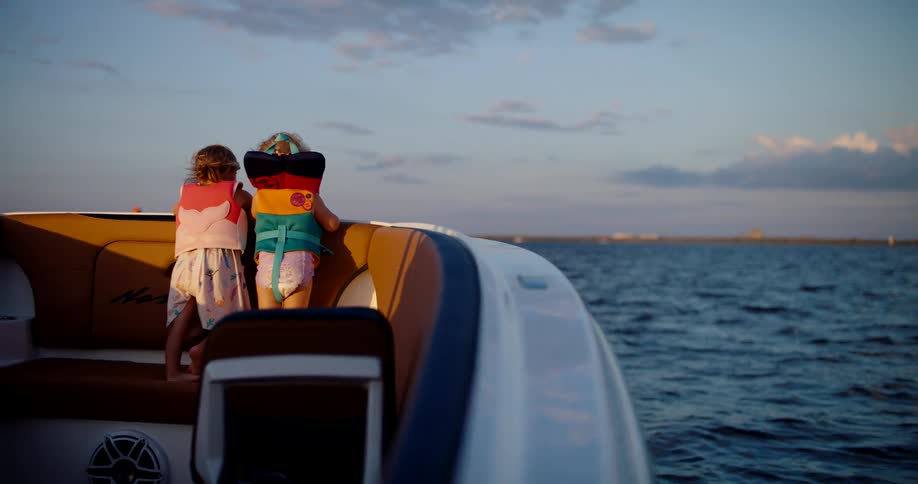 Two children wearing life jackets stand in a boat on the water
