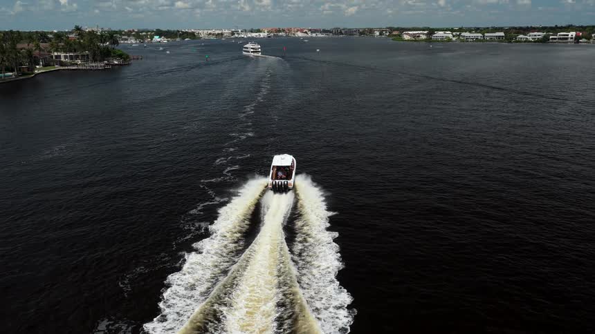 A white boat moves across the lake at midday with a town visible along the nearby shoreline
