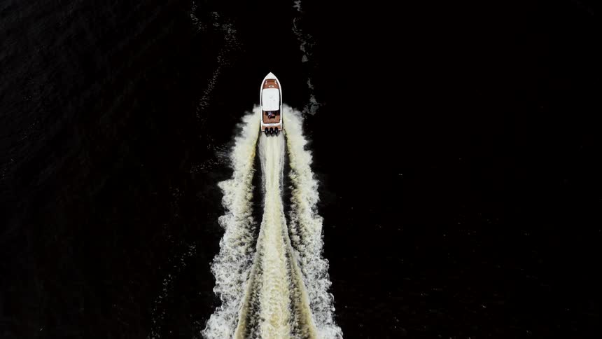 Boat cuts through dark waters leaving a trail of white foam behind
