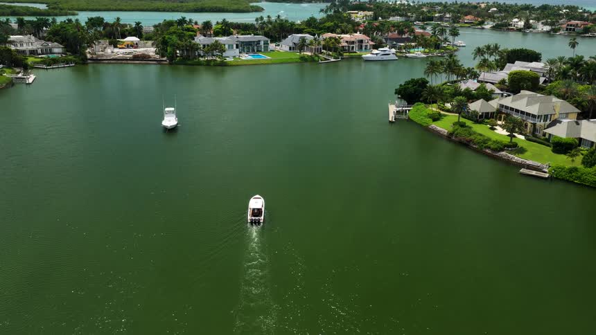 Waterfront homes surrounded by tropical greenery with boats moving through calm canal