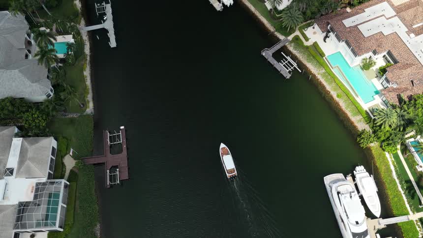 Birds eye view boat cruising through residential waterway with luxury waterfront homes