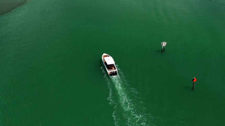 Boat sails through green waters past navigation buoys