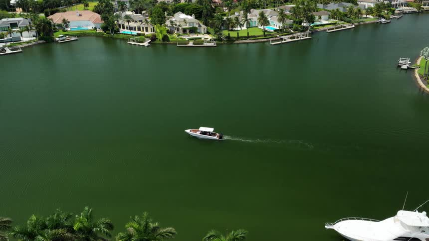 A small speedboat carves a pale wake through jadegreen canal water bordered by palmlined waterfront homes and docks