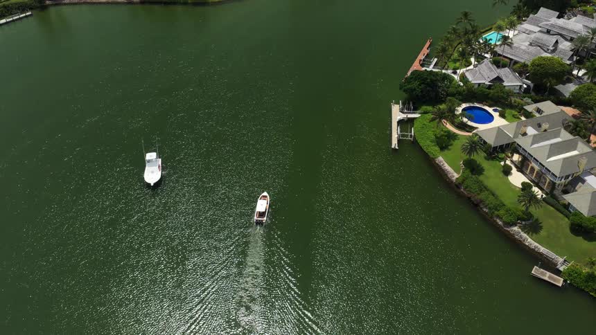 Boat sails through green waters surrounded by luxurious houses and wooded areas