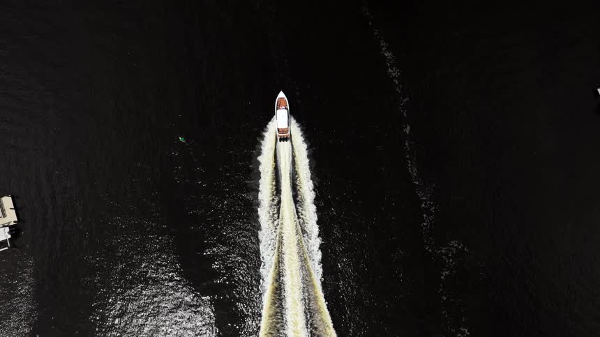 Speedboat at high speed leaves a long trail on the dark water seen from above