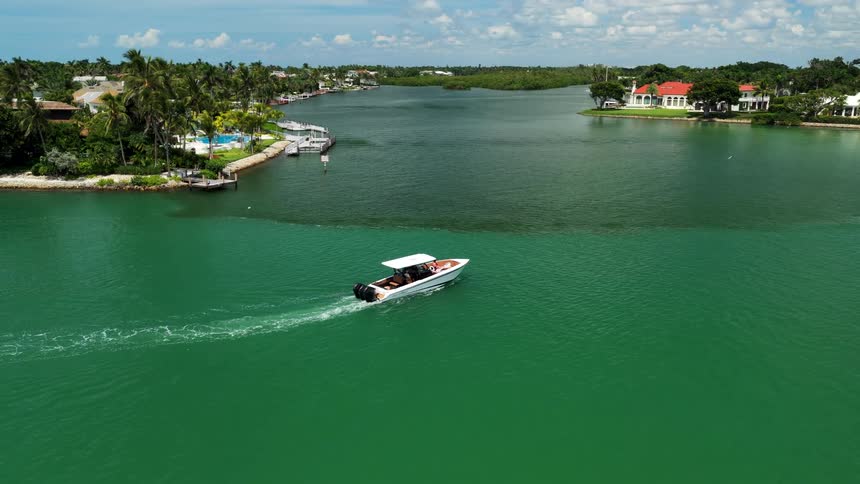 Motorboat cruising through turquoise channel between homes with docks and lush greenery
