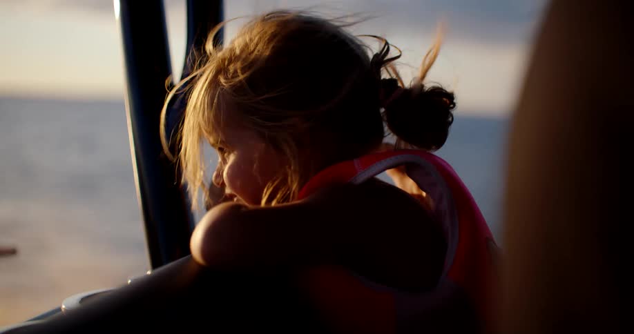 Child wearing a life jacket rests their head on their arms while looking at the sea