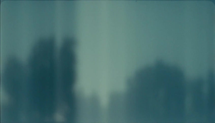 A blurred view through a window shows dark indistinct silhouettes performing a high five with light flares moving across the tealtoned surface of the glass