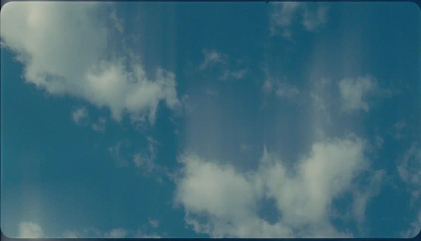 A dynamic timelapse shot shows white fluffy clouds drifting quickly across a deep blue sky with visible film grain and vertical light leaks