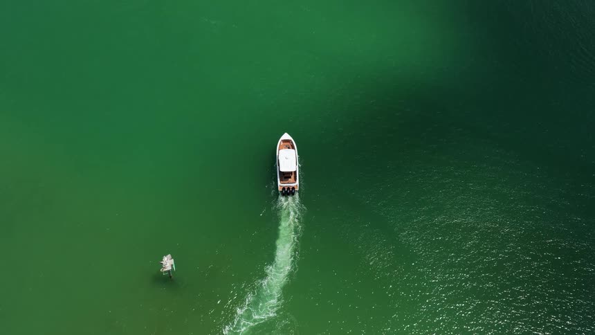 Speedboat moves forward leaving a trail on the green waters seen from above