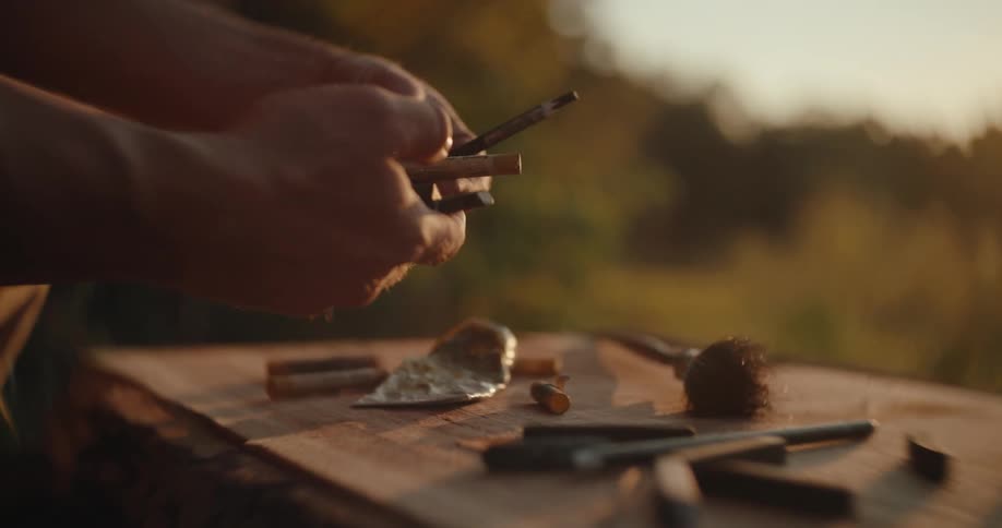 Hands hold painting tools on an outdoor table illuminated by the sunset