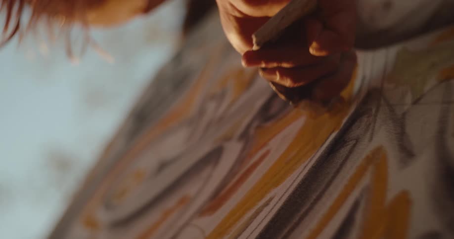 Hand holds a tube of paint while applying colorful strokes to a canvas