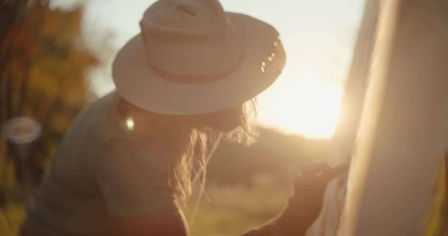 Person paints details on a large canvas outdoors under the sunset light