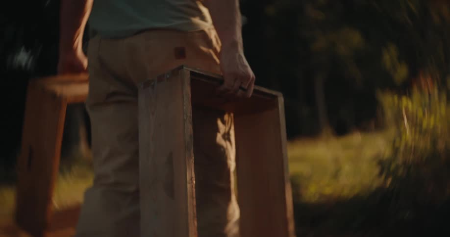 Person carries a wooden frame in an outdoor area lit by the evening light