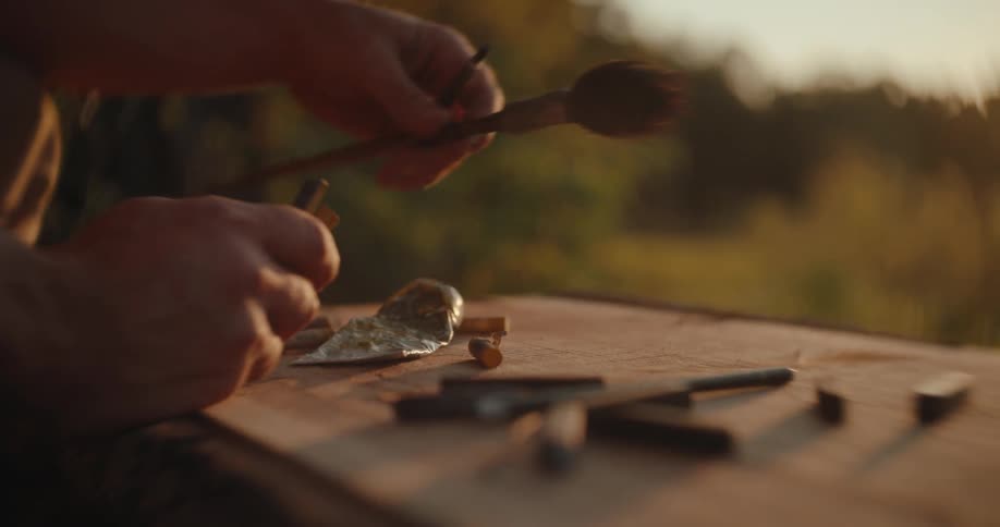 Hands handle excavation tools on a table outdoors at sunset
