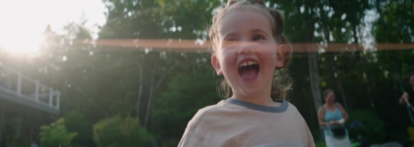 Happy little girl popping a large bubble with stick in the backyard