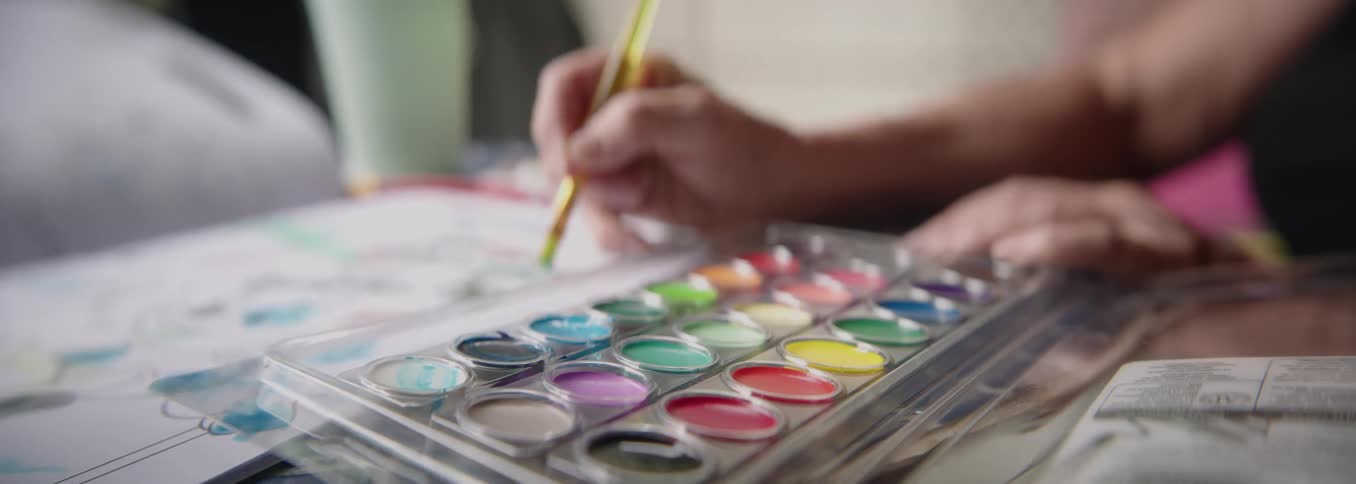 Hand selects vibrant shades from a watercolor palette to begin a painting