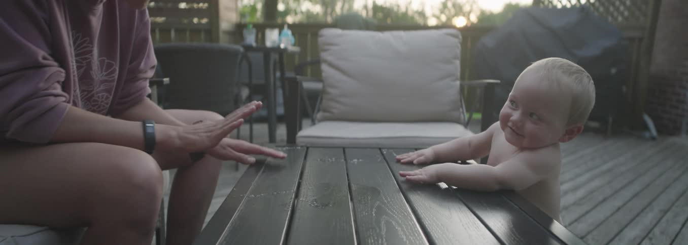Adult interacting with baby on wooden deck at dusk