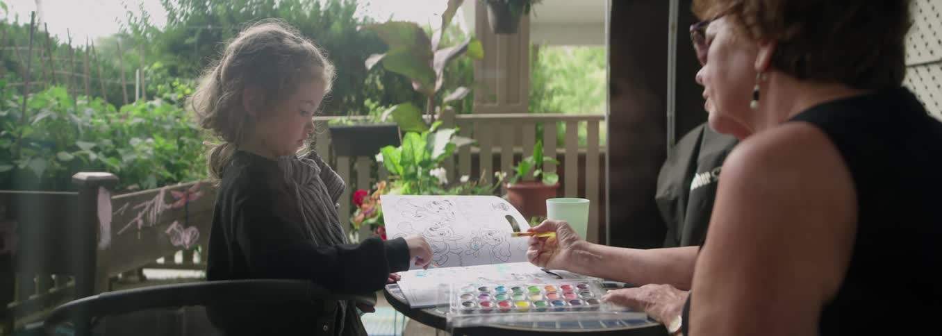 Grandmother and granddaughter watercoloring in a book outdoors in the patio