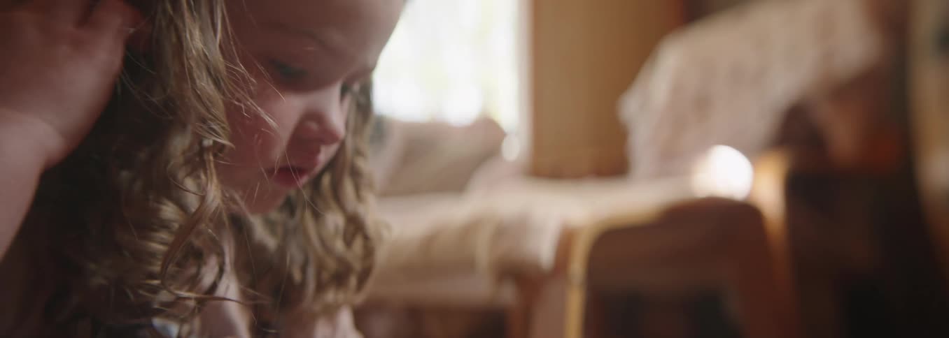 A child sits crosslegged gently turning a picture book page looking calm and absorbed in reading