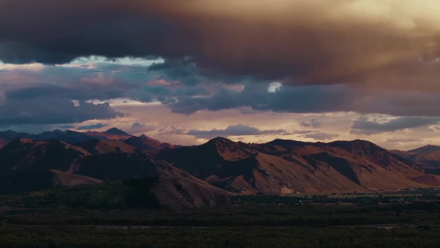 Golden evening light highlights the contours of a mountain range under a dramatic sky