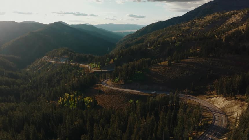 Winding road cutting through mountainous forest with autumncolored trees under golden light