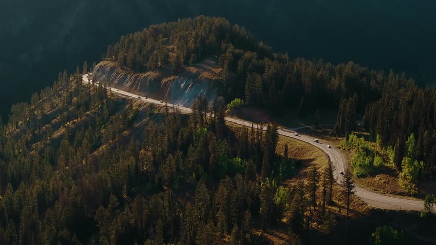 Winding road cutting through mountainous forest during sunset