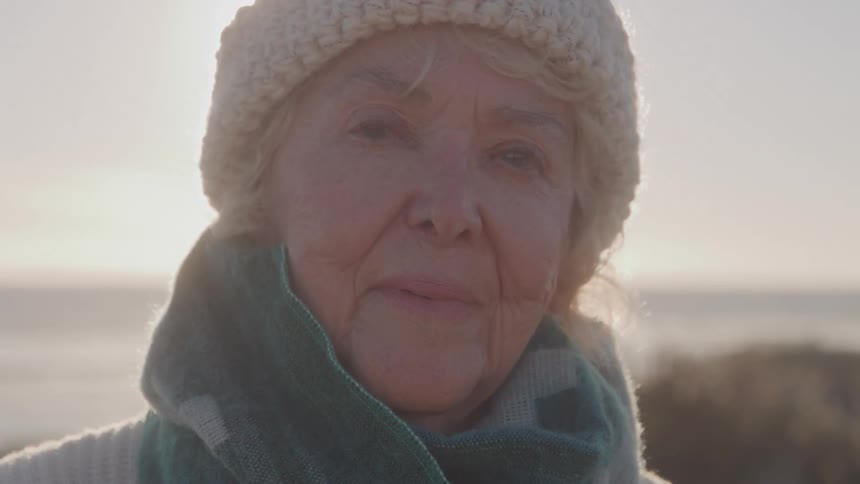 Elderly woman looks into the camera at the beach on a sunny day