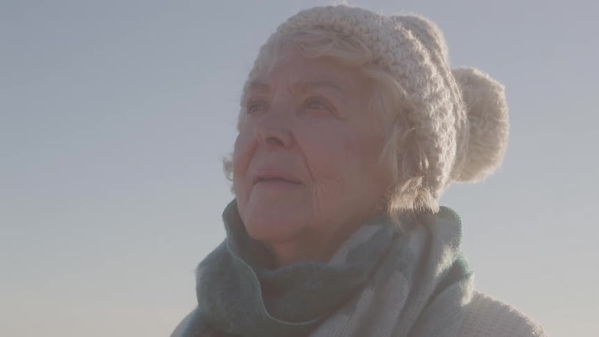 Elderly woman wearing white knit hat with pompom under blue sky