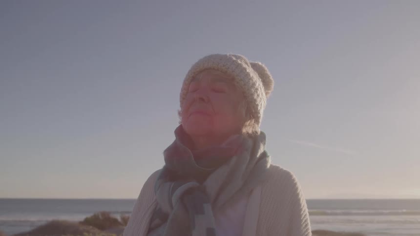 Elderly woman wearing a hat and scarf enjoys the sea breeze on a clear day