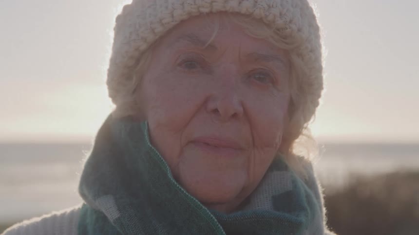 Elderly woman with hat and scarf with serene expression outdoors