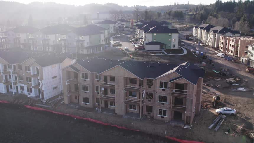 Construction workers work on buildings in an apartment complex located near forested hills on a foggy day