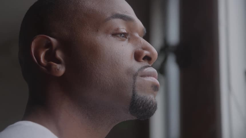 Man stands near a window and looks out of it during the daytime