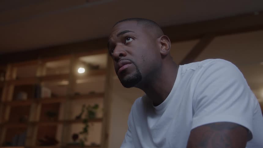 Man sitting and frowning indoors raises his head