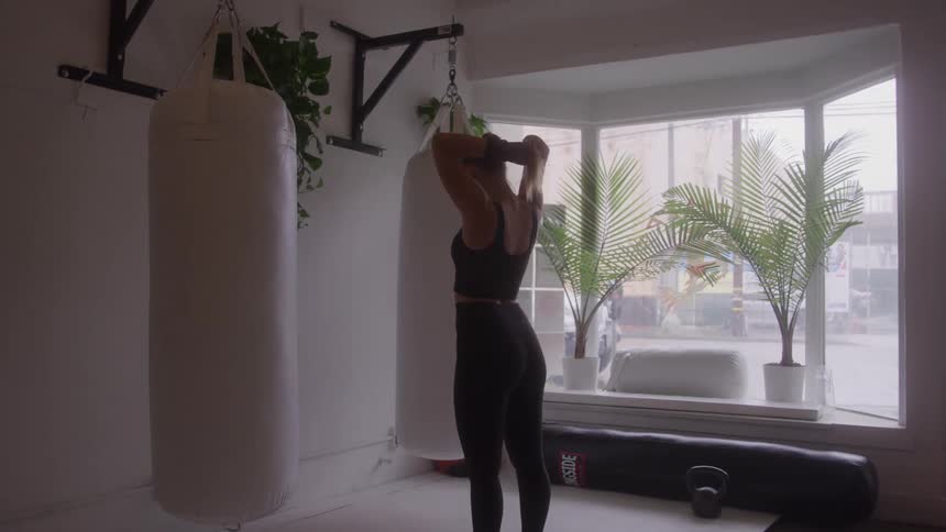 Woman stands in front of punching bag in workout space with natural light