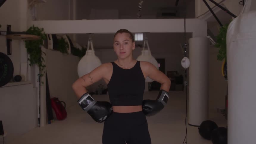 Woman wearing boxing gloves poses confidently in a bright minimalist gym