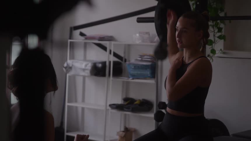 Two women in an indoor workout area with one woman stretching her arm while talking to the other woman who is partially obscured in the foreground