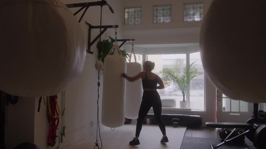 Person trains boxing alone in a gym lit by natural light