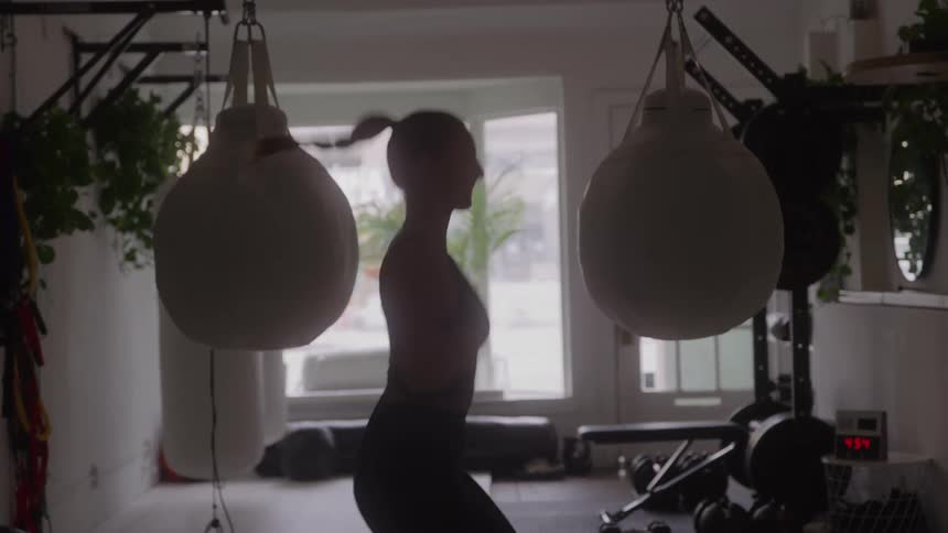 Woman jumps rope between punching bags in a bright gym